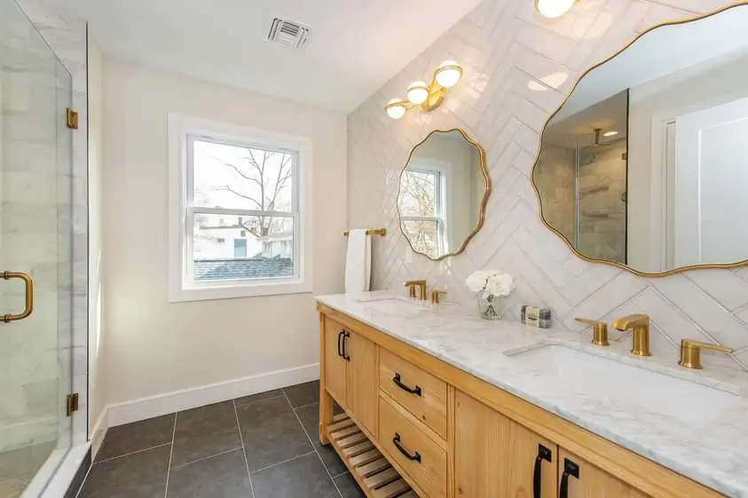 Modern bathroom with light wood vanity, double sinks with golden faucets and irregular mirrors
