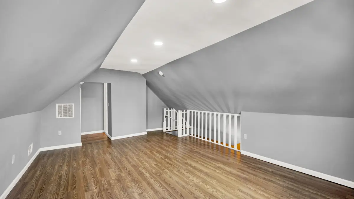 Spacious attic with light wood floor and gray sloping walls